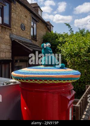 Red Royal Mail posta casella sormontata con una rana a maglia, o bombardiere di filo, nel villaggio di Hackleton, Northamptonshire, Regno Unito Foto Stock