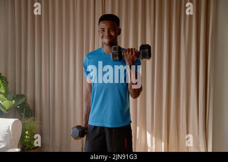Giovane afro americano nero maschio facendo bicep ricci utilizzando manubri e facendo un intenso allenamento di peso, allenarsi in palestra a casa. Foto Stock