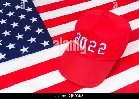 Cappello rosso TIPO MAGA con data 2022 sulla bandiera delle stelle e delle strisce degli Stati Uniti. Per le vittorie repubblicane in 2022 elezioni di Midterm degli Stati Uniti in novembre & Red Wave repubblicano degli Stati Uniti Foto Stock