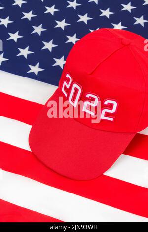 Cappello rosso TIPO MAGA con data 2022 sulla bandiera delle stelle e delle strisce degli Stati Uniti. Per le vittorie repubblicane in 2022 elezioni di Midterm degli Stati Uniti in novembre & Red Wave repubblicano degli Stati Uniti Foto Stock