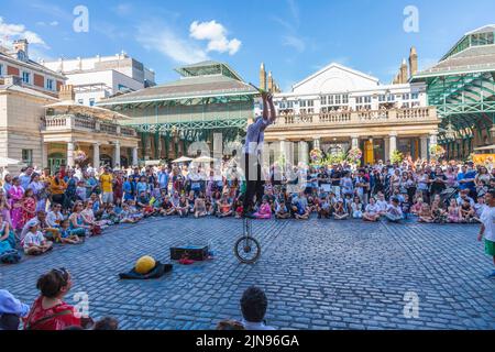 Un giocoliere maschio che intrattiene folle su un monociclo a Covent Garden, Londra, Inghilterra, Regno Unito Foto Stock