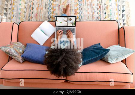 Vista ad alto angolo di una studentessa afro-americana che utilizza un computer portatile per studiare online, guardare il webinar, chiamare un insegnante tramite video, parlare con il pullman, vista dall'alto Foto Stock