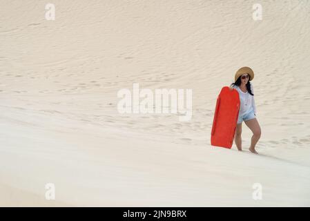 Donna che sale su una duna di sabbia con un sandboard, Kangaroo Island, South Australia Foto Stock