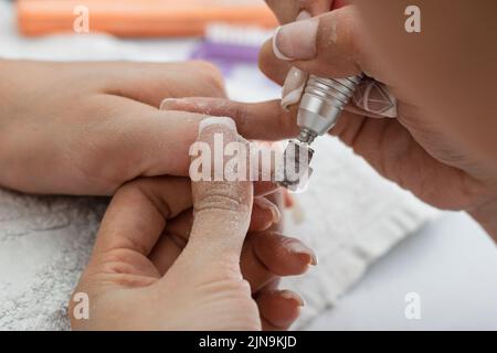 particolare delle mani di una ragazza lucidando con una lucidatrice elettrica le unghie, indossando e modellando il chiodo in poligel. ragazza che pratica con un driolo Foto Stock