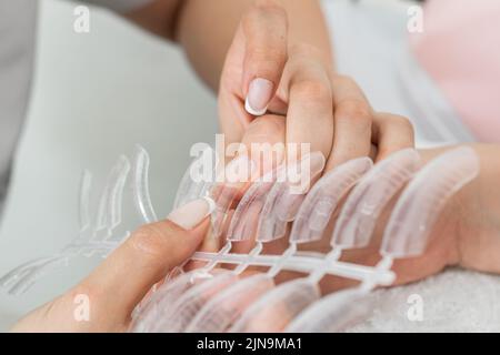 dettaglio di latina manicurista fare chiodi in poligel. prendere la misura nei falsi chiodi che hanno varie forme e dimensioni per scegliere l'uno Foto Stock