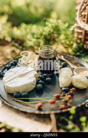 foresta pic-nic sullo sfondo di muschio e cespugli di mirtillo, formaggio e bacche su un piatto di metallo in natura Foto Stock