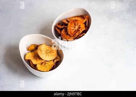 Ciotole con patatine di mele e persimmon su un tavolo di cemento Foto Stock