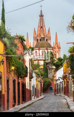 Vista mattutina della Calle Aldama, acciottolata, e della torre barocca originaria di Parroquia de San Miguel Arcangel, nel centro storico di San Miguel de Allende, Messico. Foto Stock