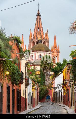 Vista mattutina della Calle Aldama, acciottolata, e della torre barocca originaria di Parroquia de San Miguel Arcangel, nel centro storico di San Miguel de Allende, Messico. Foto Stock