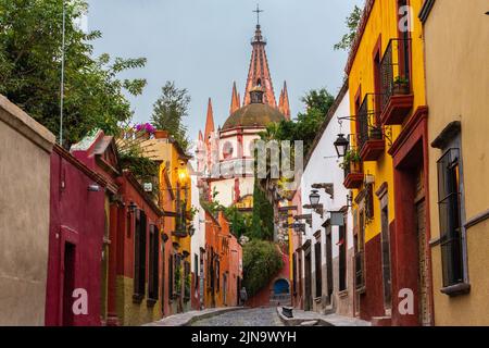 Vista mattutina della Calle Aldama, acciottolata, e della torre barocca originaria di Parroquia de San Miguel Arcangel, nel centro storico di San Miguel de Allende, Messico. Foto Stock