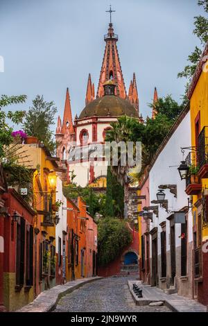 Vista mattutina della Calle Aldama, acciottolata, e della torre barocca originaria di Parroquia de San Miguel Arcangel, nel centro storico di San Miguel de Allende, Messico. Foto Stock