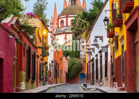 Vista mattutina della Calle Aldama, acciottolata, e della torre barocca originaria di Parroquia de San Miguel Arcangel, nel centro storico di San Miguel de Allende, Messico. Foto Stock