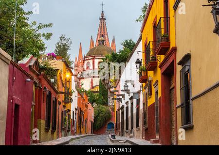 Vista mattutina della Calle Aldama, acciottolata, e della torre barocca originaria di Parroquia de San Miguel Arcangel, nel centro storico di San Miguel de Allende, Messico. Foto Stock