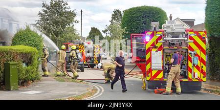 Servizio antincendio e di soccorso Essex vigili del fuoco vigili del fuoco che spruzzano acqua sul fuoco casa vista posteriore del motore di vigili del fuoco di brigata in strada residenziale Inghilterra Regno Unito Foto Stock