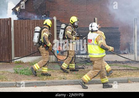 Due vigili del fuoco vigili del fuoco abbigliamento protettivo e apparecchi respiratori in procinto di cercare all'interno di casa bruciante edificio incendio Inghilterra UK Foto Stock
