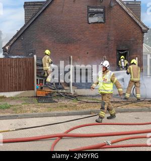 Servizio antincendio e di soccorso Essex vigili del fuoco in abbigliamento protettivo lavoro pericoloso e pericoloso su fuoco domestico che lavora con respiratore Inghilterra UK Foto Stock