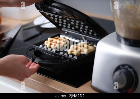 La donna prepara waffle belgi fatti in casa in cucina Foto Stock