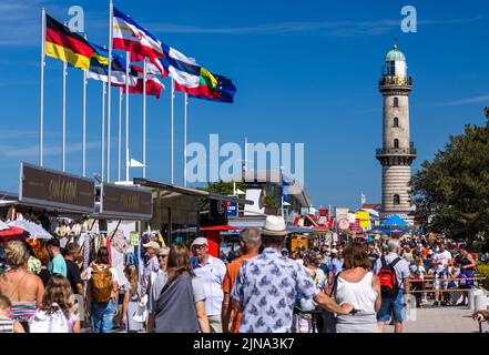 Rostock, Germania. 10th ago 2022. I turisti e i visitatori del giorno si trovano sul lungomare di fronte al faro di Warnemünde. Molti visitatori approfittano del clima caldo e soleggiato per le escursioni in spiaggia sulla costa del Mar Baltico. Credit: Jens Büttner/dpa/Alamy Live News Foto Stock