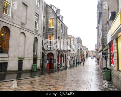 Guardando giù una stretta strada di mattoni, fiancheggiata da edifici di granito, ad Aberdeen, Scozia, bagnato dopo una rapida doccia a pioggia Foto Stock