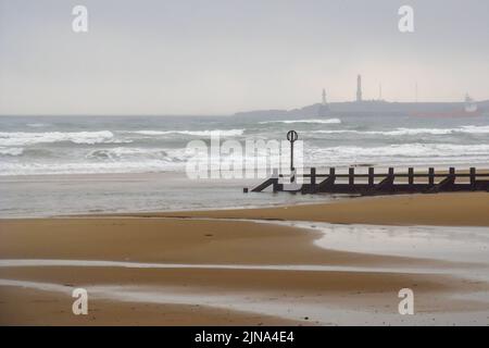 Vista sulla deserta spiaggia sabbiosa di Aberdeen, con il faro nella nebbia sullo sfondo Foto Stock