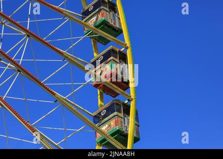 Ruota panoramica, capsule o carrozze su un colorato giro in funfair contro il cielo blu chiaro Foto Stock