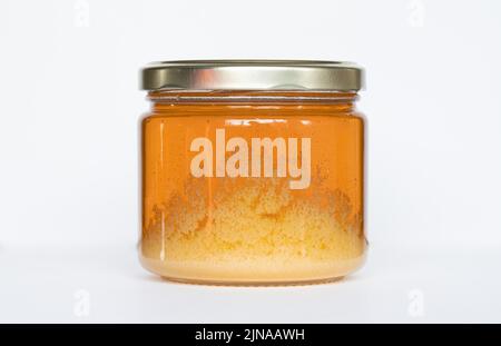Vasetto di miele che inizia a cristallizzare su fondo bianco Foto Stock