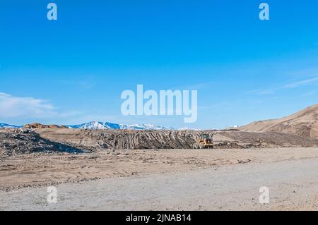 Un bulldozer giallo intatto è parcheggiato in lontananza in una discarica o discarica di rifiuti solidi attivi. Foto Stock