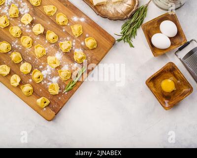 Vista dall'alto. Su un tagliere di legno, ravioli fatti in casa con ripieno di carne, ingredienti per cucinare su sfondo bianco. Non ci sono persone in Foto Stock