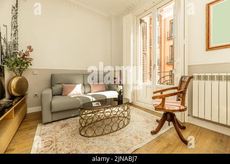 Soggiorno in appartamento con tavolo laterale in metallo e vetro, divano a due posti rivestito in tessuto grigio e balcone con porte bianche Foto Stock