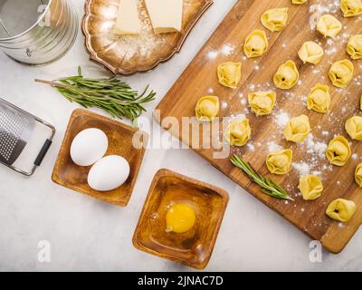 Su sfondo bianco, ravioli fatti in casa su un tagliere, cosparsi di farina, molti ingredienti, utensili da cucina. Ricette per la cucina casalinga. Co Foto Stock