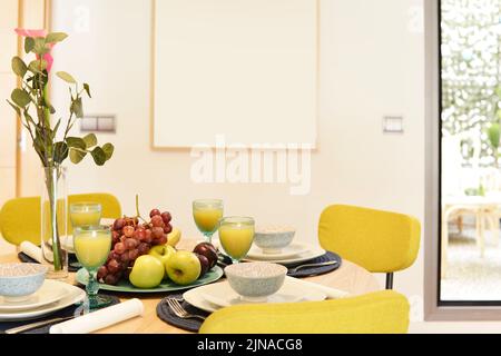 Centrotavola con un vassoio di frutta fresca, un vaso decorativo, un mazzo di uva e bicchieri di succo d'arancia Foto Stock