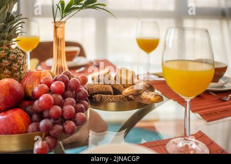 Centrotavola con vassoio di frutta fresca, grappolo d'uva, molti muffin e dolci, vaso decorativo, mele rosse, prugne mature e bicchieri di succo d'arancia Foto Stock