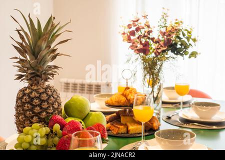 Centrotavola con vassoio di frutta fresca, grappolo d'uva, tanti muffin e caramelle, vaso decorativo, mele verdi, fragole, croissant, prugna matura Foto Stock