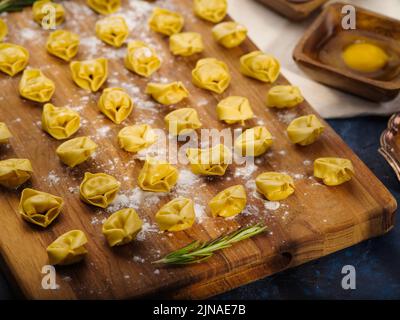 Appetitosi ravioli fatti in casa, gnocchi con ripieno di carne su un tagliere su uno sfondo blu scuro. Ristorante e ricette di cucina casalinga. Cucina b Foto Stock