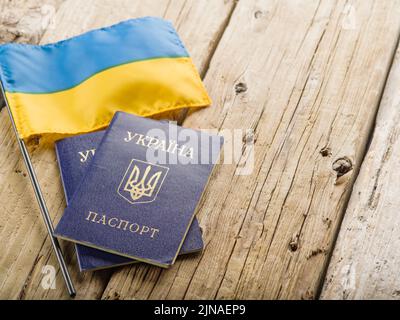 Su un tavolo di legno è una piccola bandiera dell'Ucraina e due passaporti biometrici ucraini. Viaggi, turismo, tempo libero, lavoro, rifugiati. Guerra in Ucraina, em Foto Stock