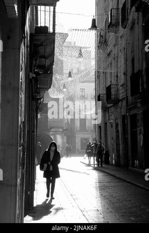 Un'immagine in scala di grigi verticale delle persone che camminano lungo la strada. Girona, Spagna. Foto Stock