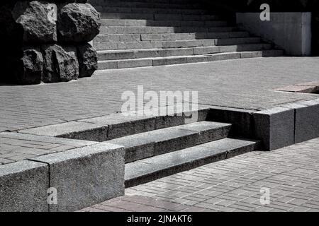 Gradini di granito grigio nel mezzo di piastrelle di pietra modello di mattoni pavimento strada, paesaggio urbano con passerella vicino all'edificio e scale in giorno di sole, vista sul pavimento Foto Stock