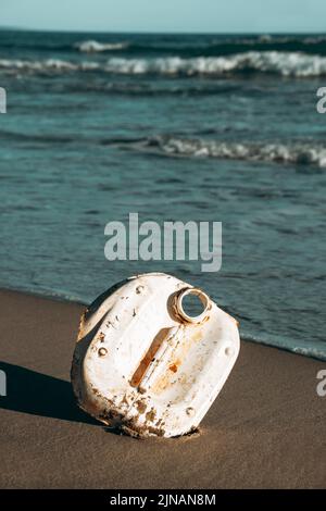 un pezzo di una bottiglia di plastica bianca usata sulla sabbia bagnata di una spiaggia, riportata in riva al mare dall'oceano Foto Stock