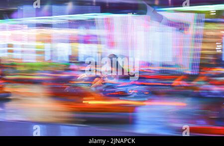 Esposizione notturna lunga che segue un autoscontri che corre veloce in pista con numerose luci. Foto Stock