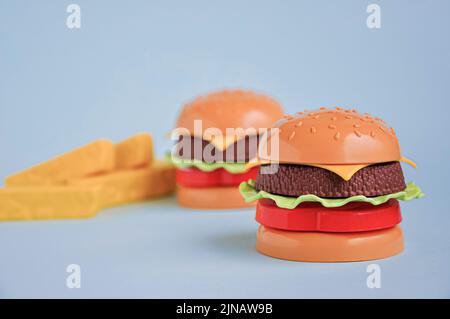 Hamburger giocattolo in plastica per bambini con insalata, pomodoro, carne e patatine fritte sul blu. Concetto di alimento artificiale nocivo. Malsano. Non organico. Non utile Foto Stock