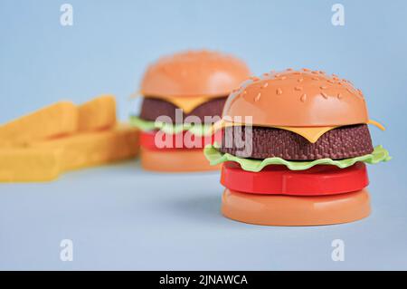 Hamburger giocattolo in plastica per bambini con insalata, pomodoro, carne e patatine fritte sul blu. Concetto di alimento artificiale nocivo. Malsano. Non organico. Non utile Foto Stock