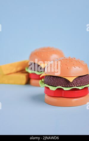 Hamburger giocattolo in plastica per bambini con insalata, pomodoro, carne e patatine fritte sul blu. Concetto di alimento artificiale nocivo. Malsano. Non organico. Non utile Foto Stock