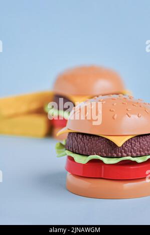 Hamburger giocattolo in plastica per bambini con insalata, pomodoro, carne e patatine fritte sul blu. Concetto di alimento artificiale nocivo. Malsano. Non organico. Non utile Foto Stock