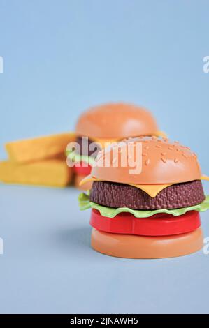 Hamburger giocattolo in plastica per bambini con insalata, pomodoro, carne e patatine fritte sul blu. Concetto di alimento artificiale nocivo. Malsano. Non organico. Non utile Foto Stock