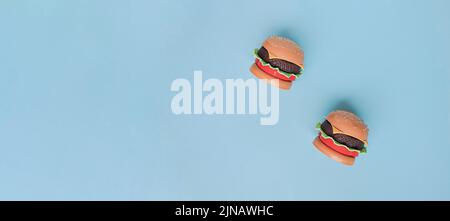 Hamburger giocattolo in plastica per bambini con insalata, pomodoro, carne sul blu. Concetto di alimento artificiale nocivo. Malsano. Non organico. Non utile. In esame oggi Foto Stock