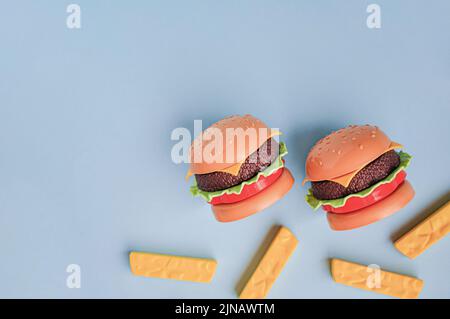 Hamburger giocattolo in plastica per bambini con insalata, pomodoro, carne e patatine fritte sul blu. Concetto di alimento artificiale nocivo. Malsano. Non organico. Non utile Foto Stock