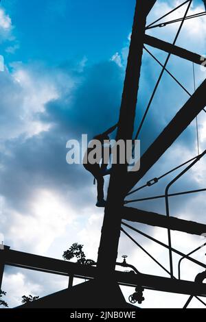 Silhouette nera di un uomo che sale su una torre metallica. Silhouette di un uomo che è in cima ad una struttura di metallo arrampicata. Ombra di un uomo che si arrampica. Foto Stock