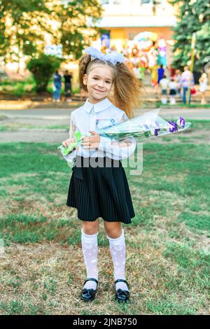 Lysychansk, Ucraina. 1 settembre 2021 - una ragazza con un bouquet di fiori in una blusa bianca con archi sullo sfondo della scuola durante il Foto Stock