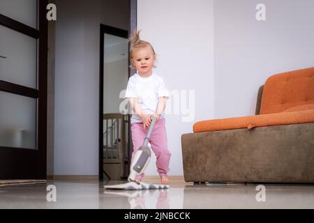 Piccola figlia pulizia in casa, bambino spolverare, carino piccola helper ragazza lavaggio pavimento con mop, la famiglia felice pulisce la camera, Foto Stock