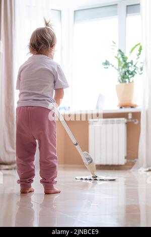 Piccola figlia pulizia in casa, bambino spolverare, carino piccola helper ragazza lavaggio pavimento con mop, la famiglia felice pulisce la camera, Foto Stock